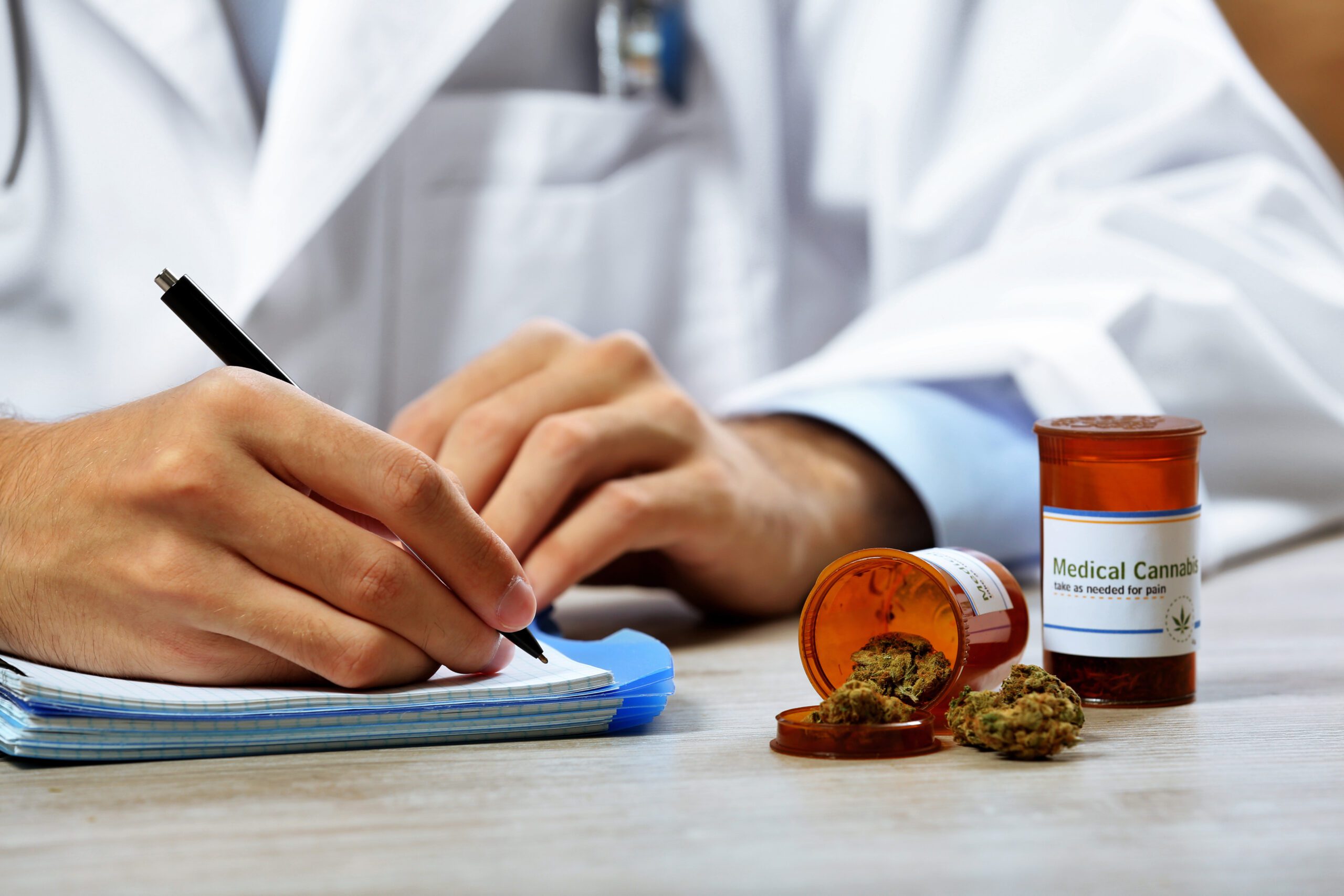 Doctor writing on prescription blank and bottle with medical cannabis on table close up